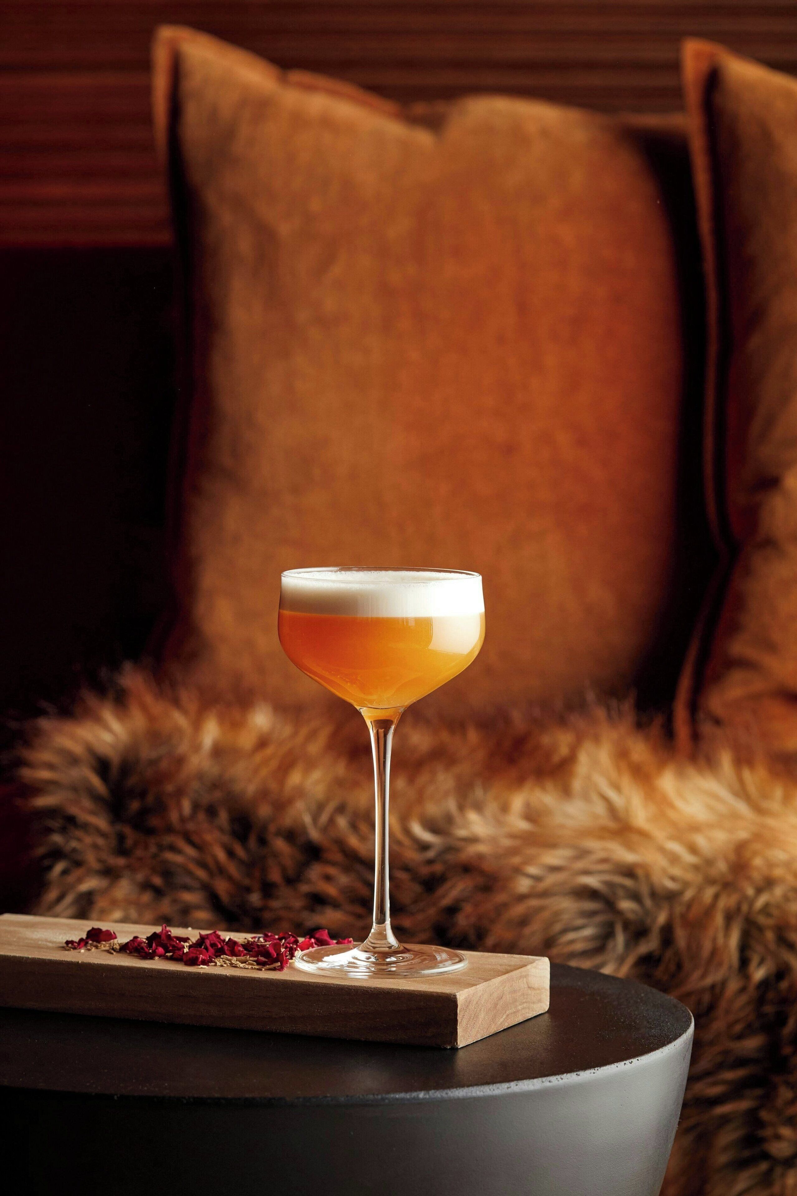 Un verre à cocktail posé sur un dessous de verre en bois, sur une table ronde.
