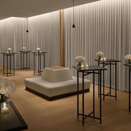 Un interior moderno con un sofá, mesas con velas y un fondo de cortina blanca.
