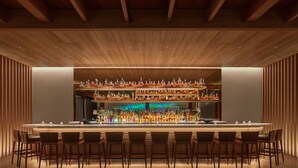 Un bar moderno con una barra larga, varios estantes llenos de botellas y varios taburetes.