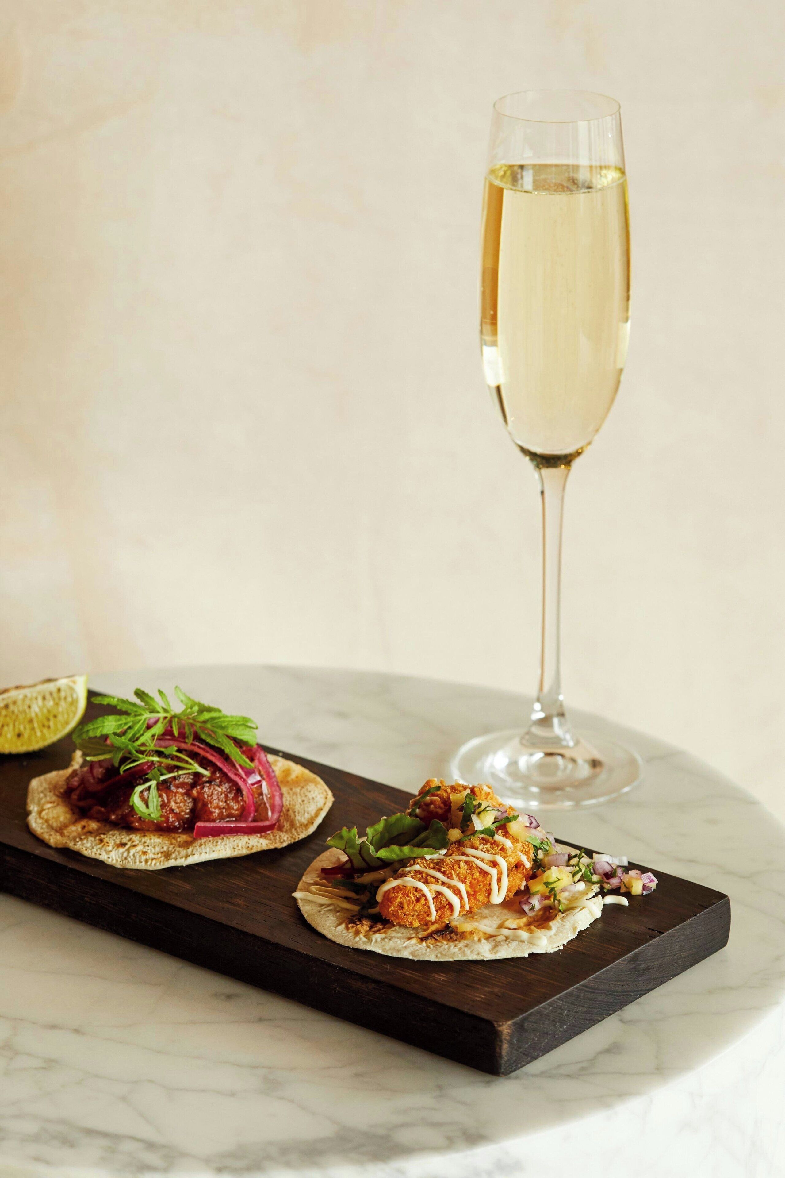 Een tafel met twee kleine porties eten en een glas champagne.