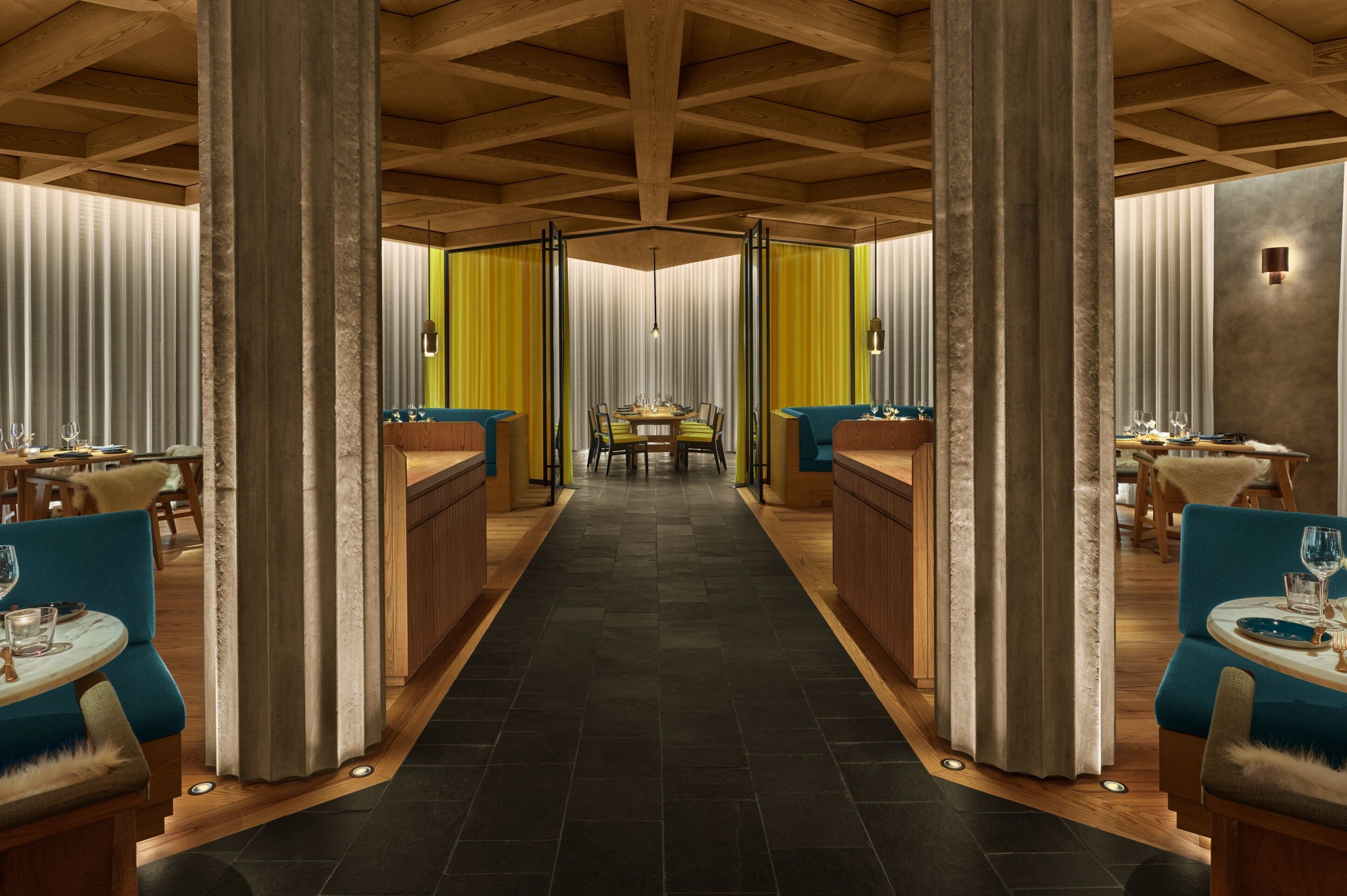 A restaurant with a central dining area, wooden beams on the ceiling, and curtains on the walls.