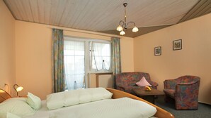 A hotel room with a bed, two chairs, a table, and a window with curtains. - Pension Martinus (Neustadt an der Donau)