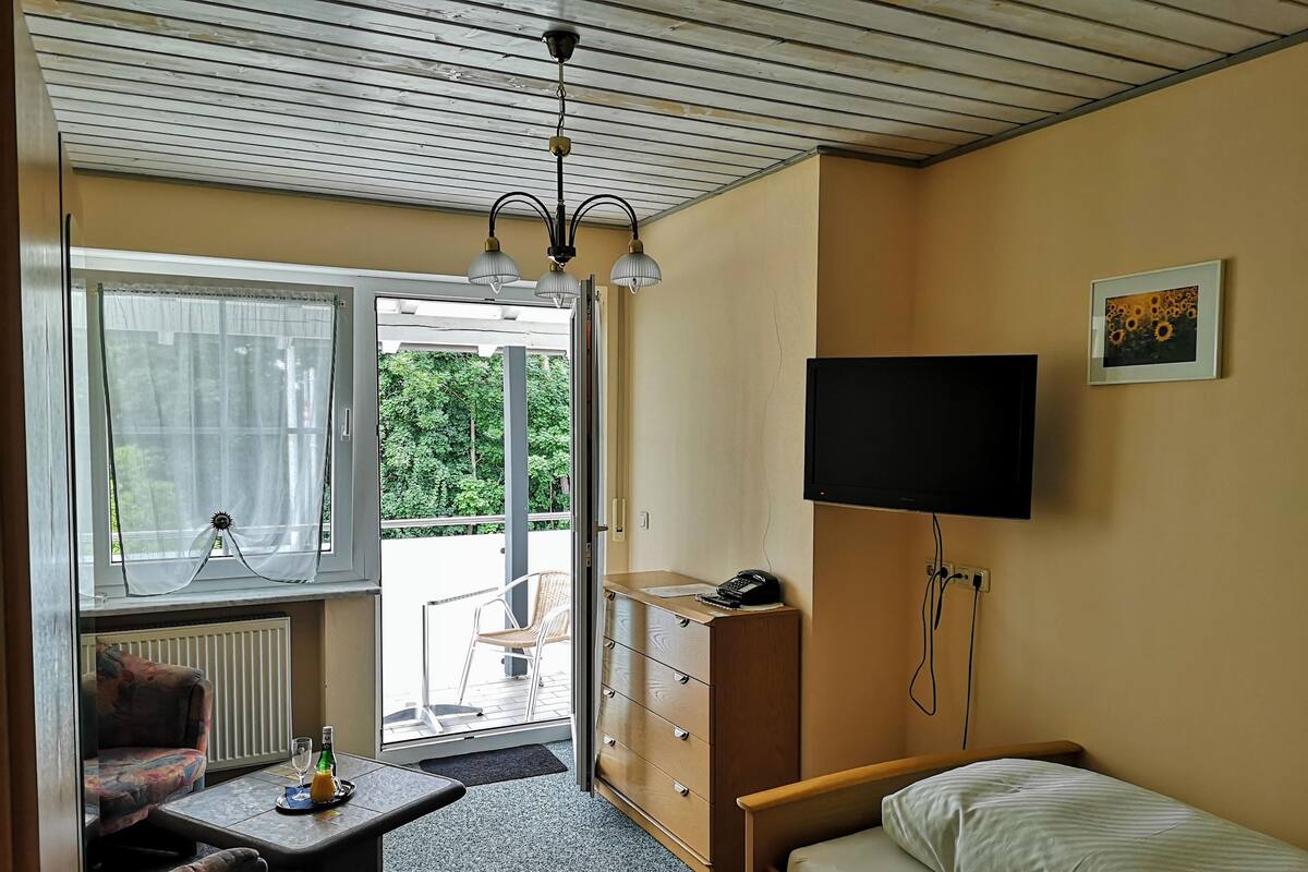 A compact room with a bed, a desk with a chair, a television, and a window with curtains.