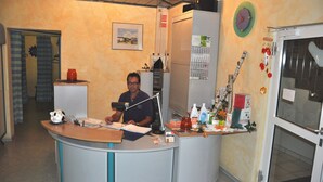 A reception desk with a man seated behind it, a calendar, a clock, and various items on the counter. - Pension Martinus (Neustadt an der Donau)