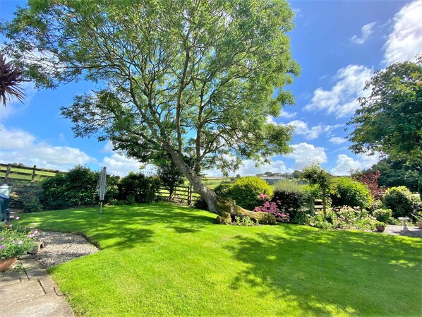 A well-maintained garden with a large tree, a stone pathway, and various shrubs and flowers.