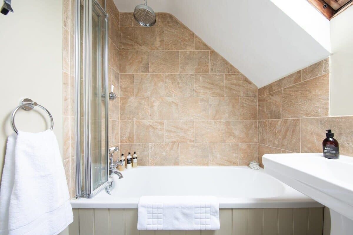 Un baño con cabina de ducha de vidrio, bañera blanca y azulejos color beige.