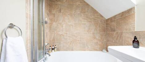 Un baño con cabina de ducha de vidrio, bañera blanca y azulejos color beige.