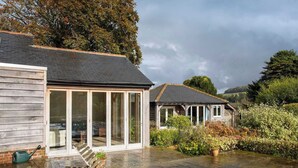 A wooden house with large glass windows, a covered patio, and a garden with various plants. - Charming Cottage for 10 in Heart of South Downs (Eartham)