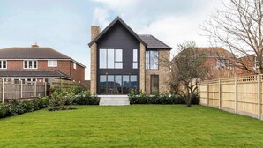 A modern two-story house with a dark facade, large windows, and a well-maintained lawn. - Stylish new home with parking - king beds, garden (Chichester)