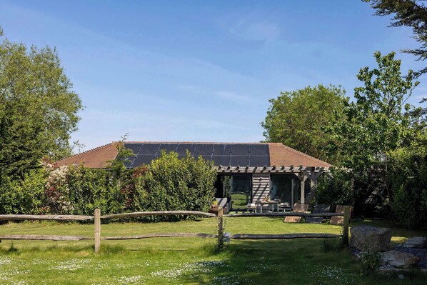 Une maison dotée d’un toit équipé de panneaux solaires, d’un patio couvert avec des meubles d’extérieur et d’une cour clôturée.