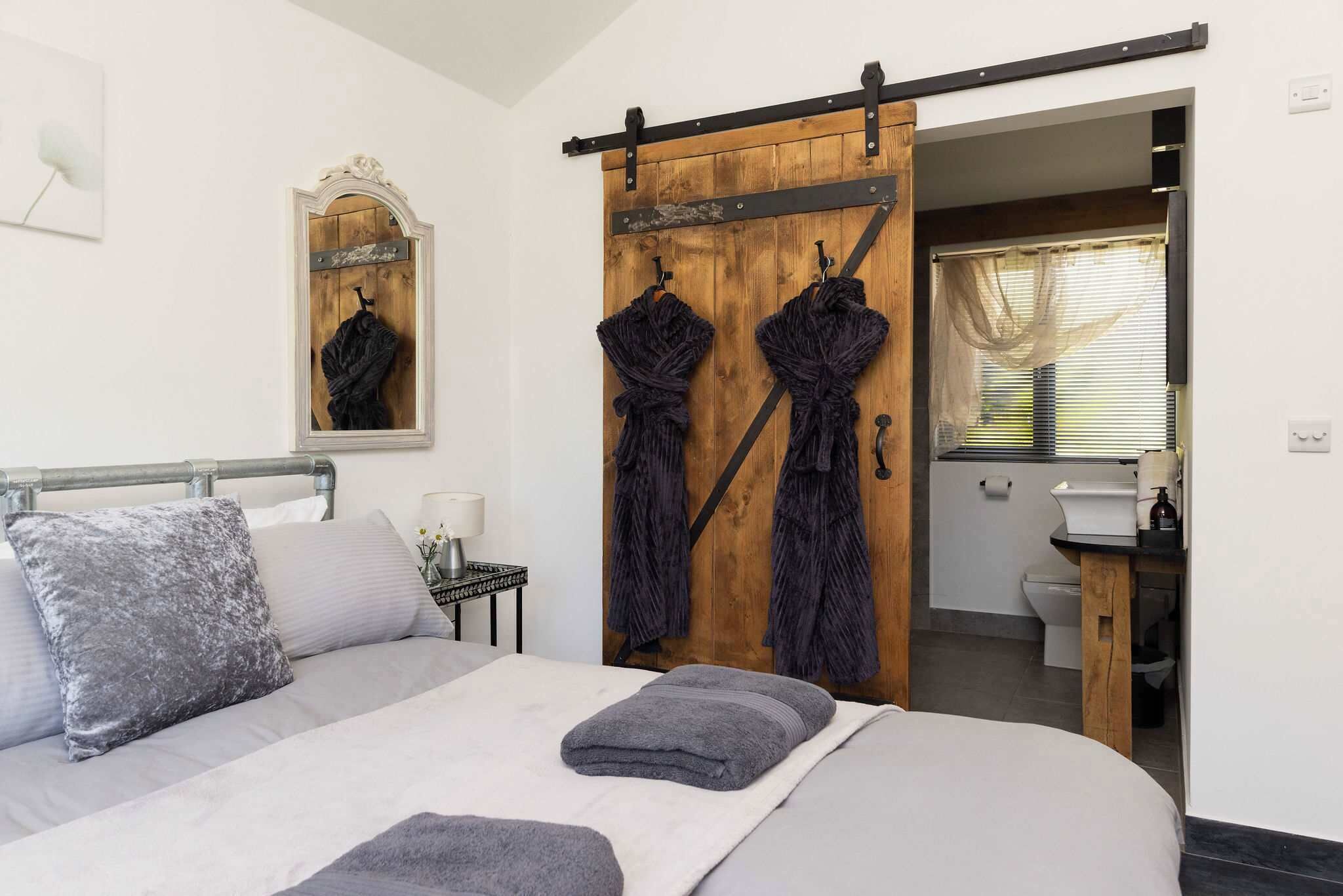 A bedroom with a bed, a wooden sliding door, a mirror, and a bathroom visible through the door.