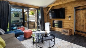 A cozy room with a sofa, two round tables, a flat-screen TV, and a sliding glass door leading to an outdoor area. - Rural Lodge Retreat with Hot Tub (Chichester)
