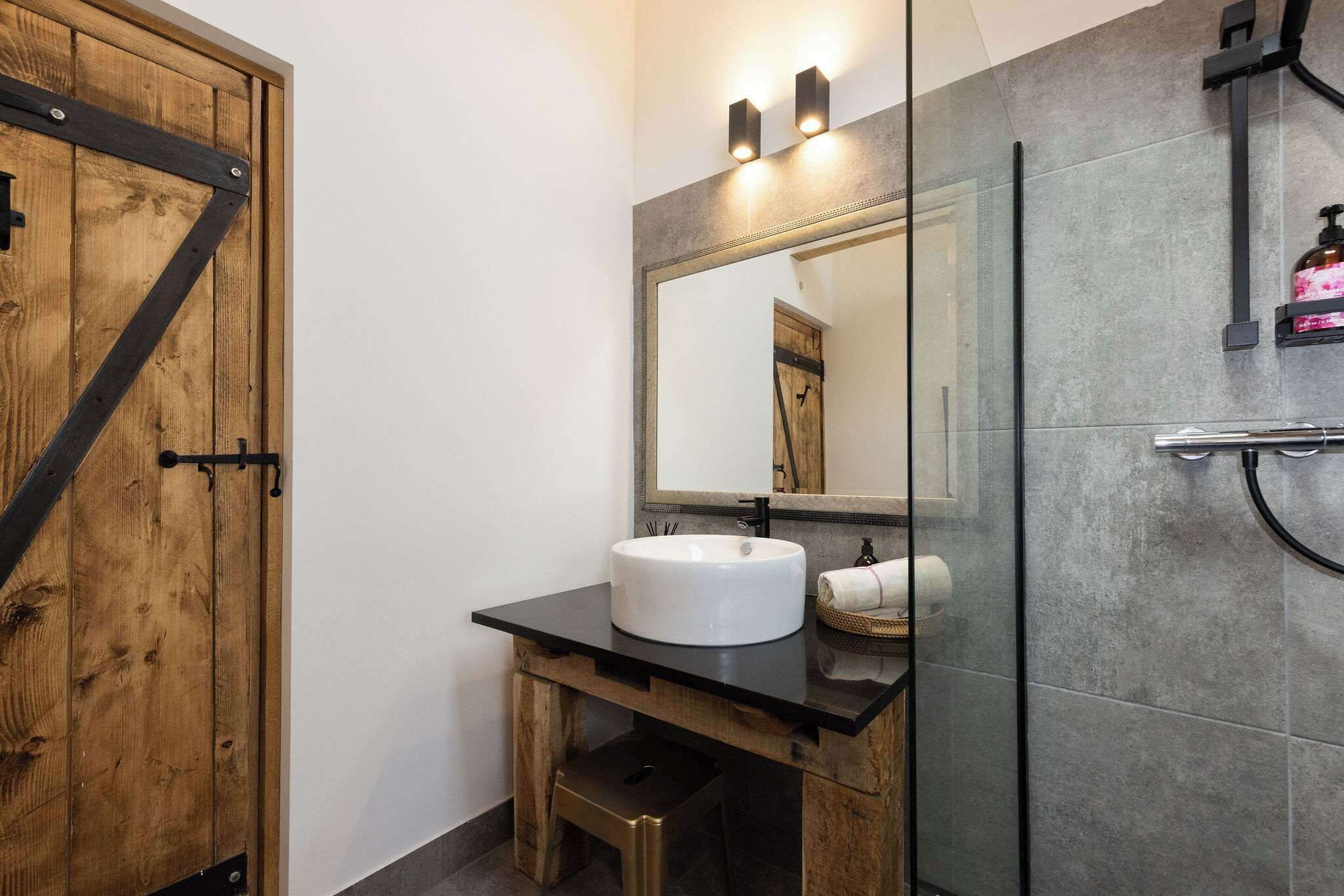 A bathroom with a wooden door, a white sink, a mirror, and a shower area.