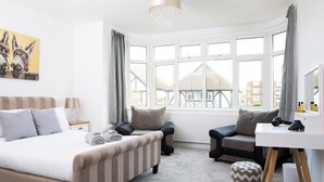 A bedroom with a bed, a desk, a chair, and a window with a view of buildings. - Spacious House for 10 Near Town & Beach (Bognor Regis)