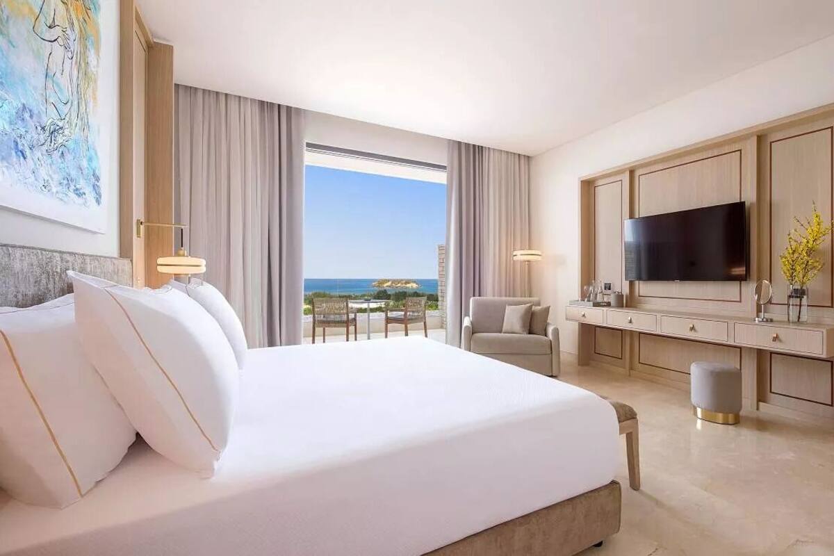 Une chambre d’hôtel avec un grand lit, une télévision, un bureau avec une chaise et une vue sur l’océan.