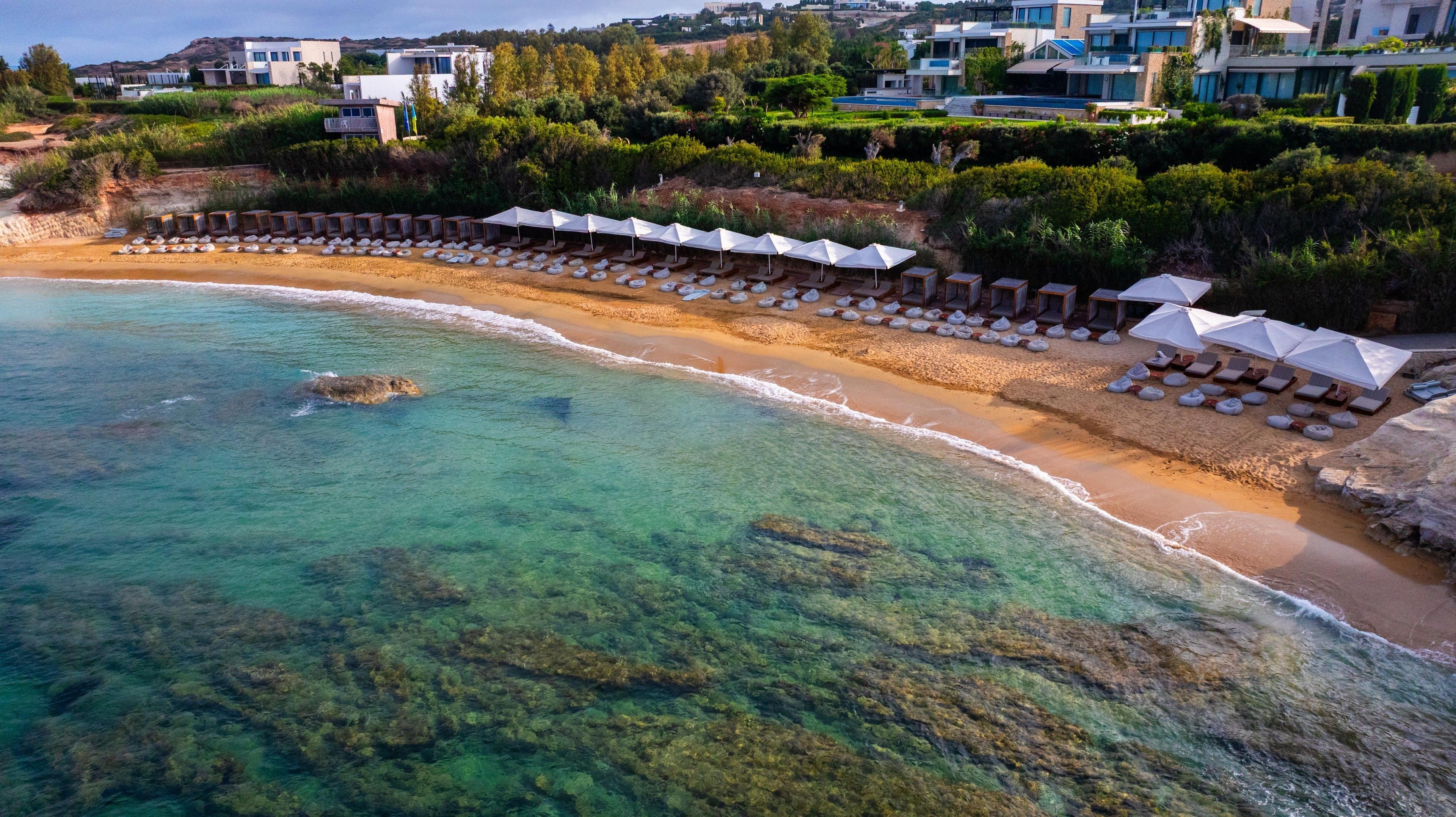 A coastal resort with a beach, lounge chairs, umbrellas, and a clear view of the sea.