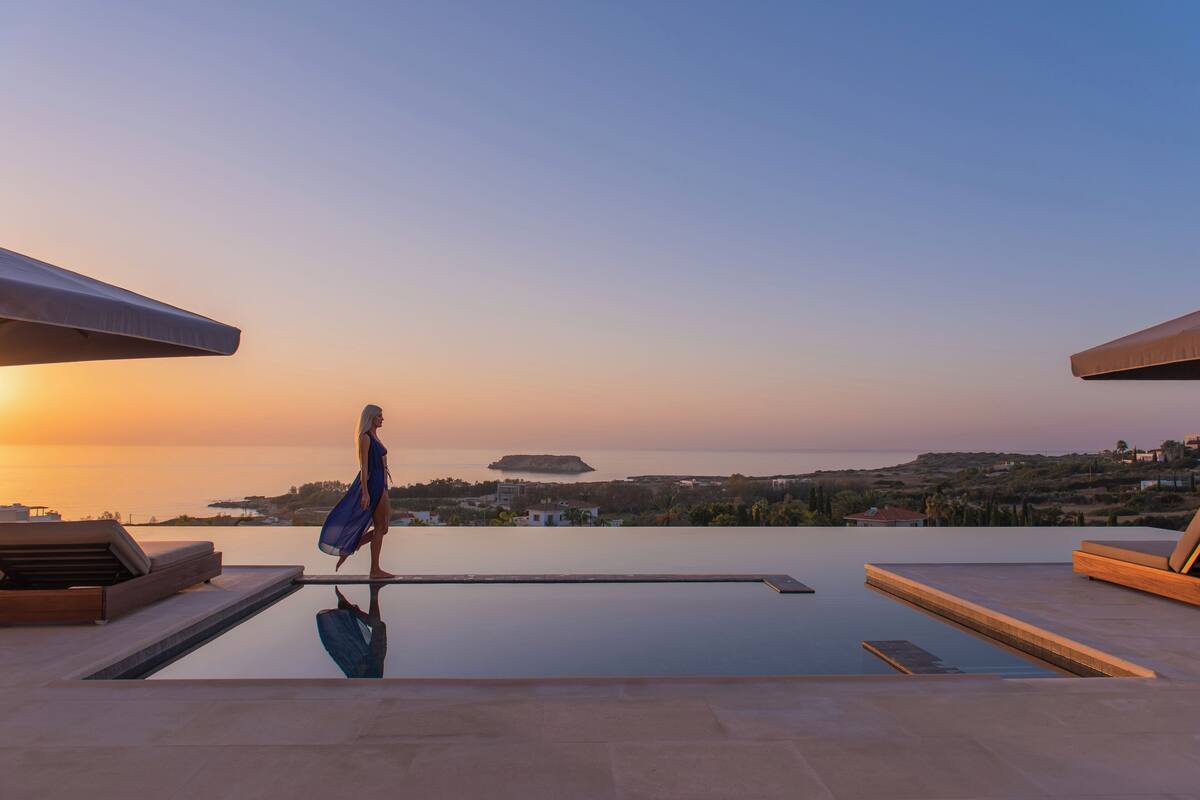 Un espace aménagé au bord de la piscine, offrant une vue sur la mer et une île lointaine au coucher du soleil.