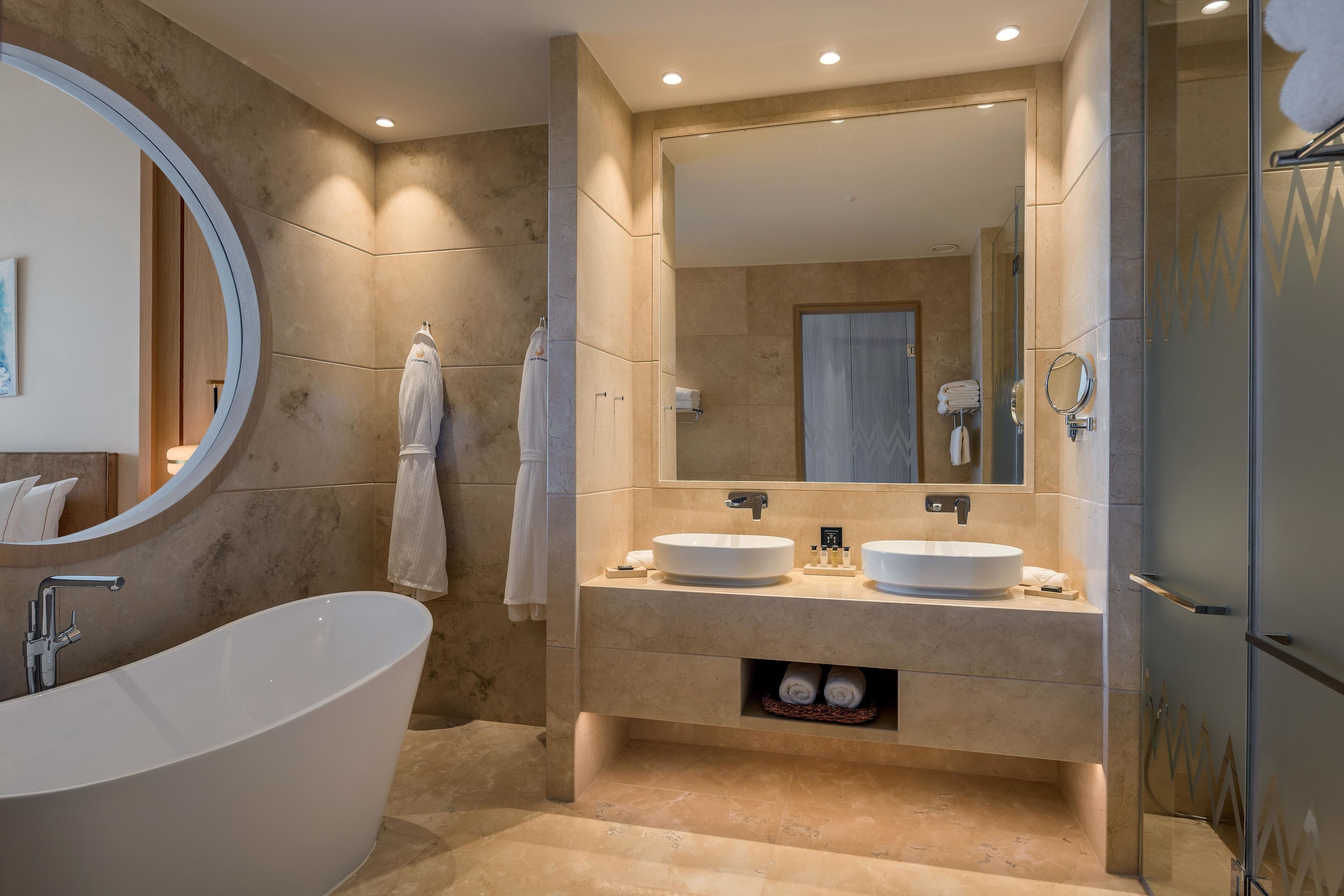 Un baño moderno con una bañera independiente, dos lavamanos, un espejo grande y una zona de ducha con mampara de cristal.