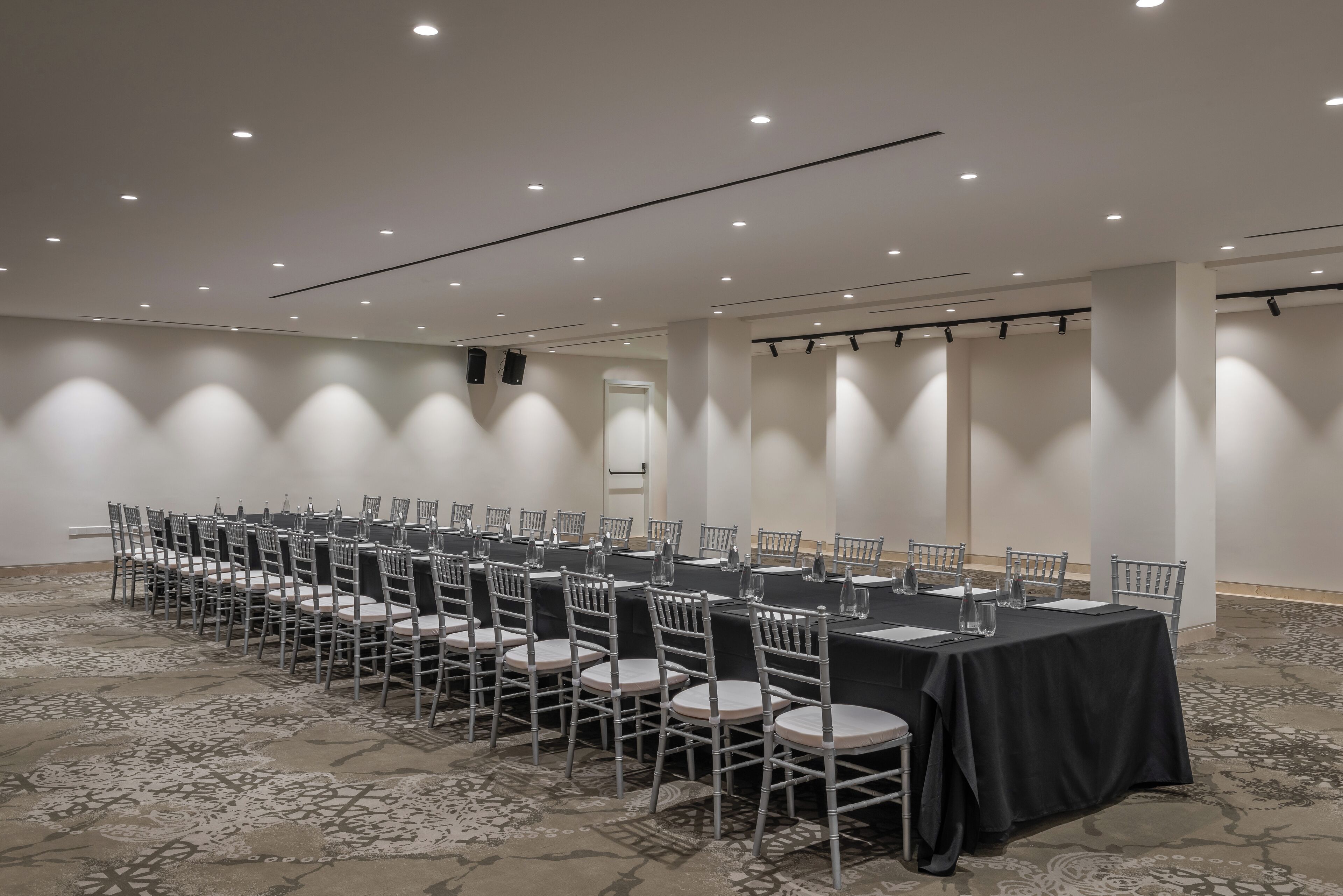 Een vergaderzaal met een lange tafel, stoelen en een vloerbedekking.