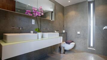 A modern bathroom with a large mirror, two sinks, a toilet, and a trash bin.