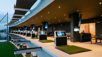 A modern indoor golf driving range with multiple stations, a seating area, and a pool.