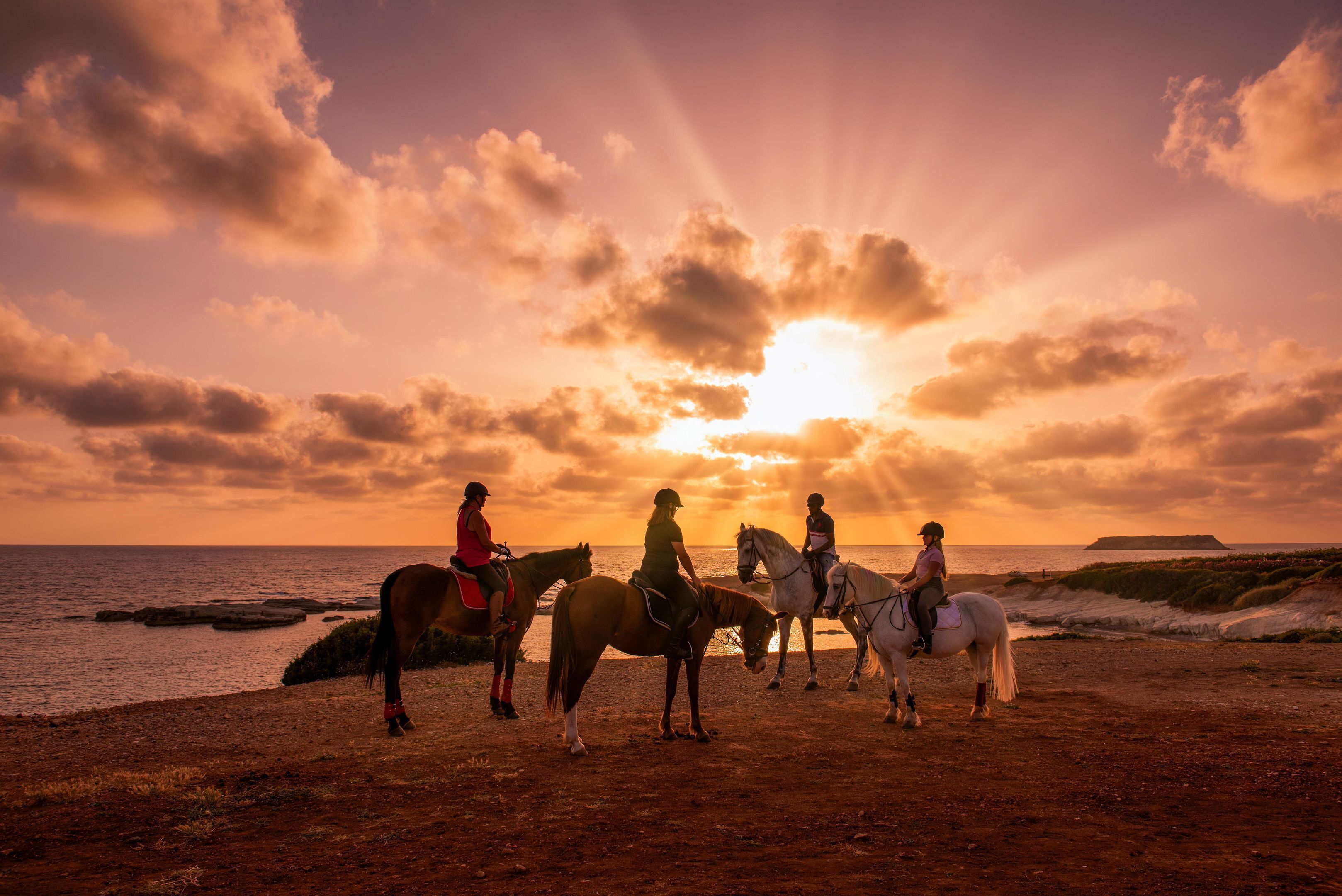 Une scène de coucher de soleil où l’on voit trois personnes à cheval sur une plage.