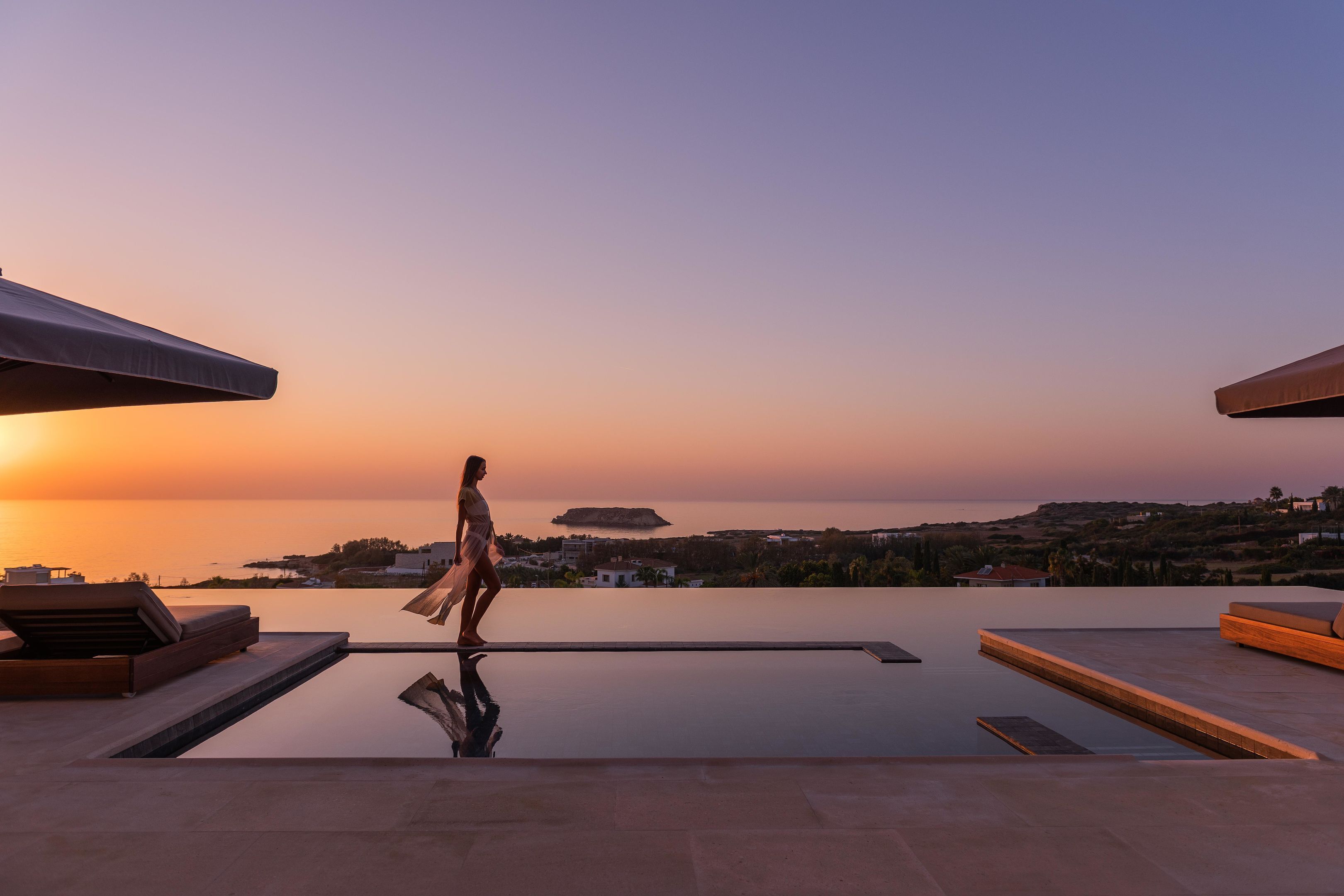 Una mujer caminando sobre una piscina en la azotea, con vista al atardecer.