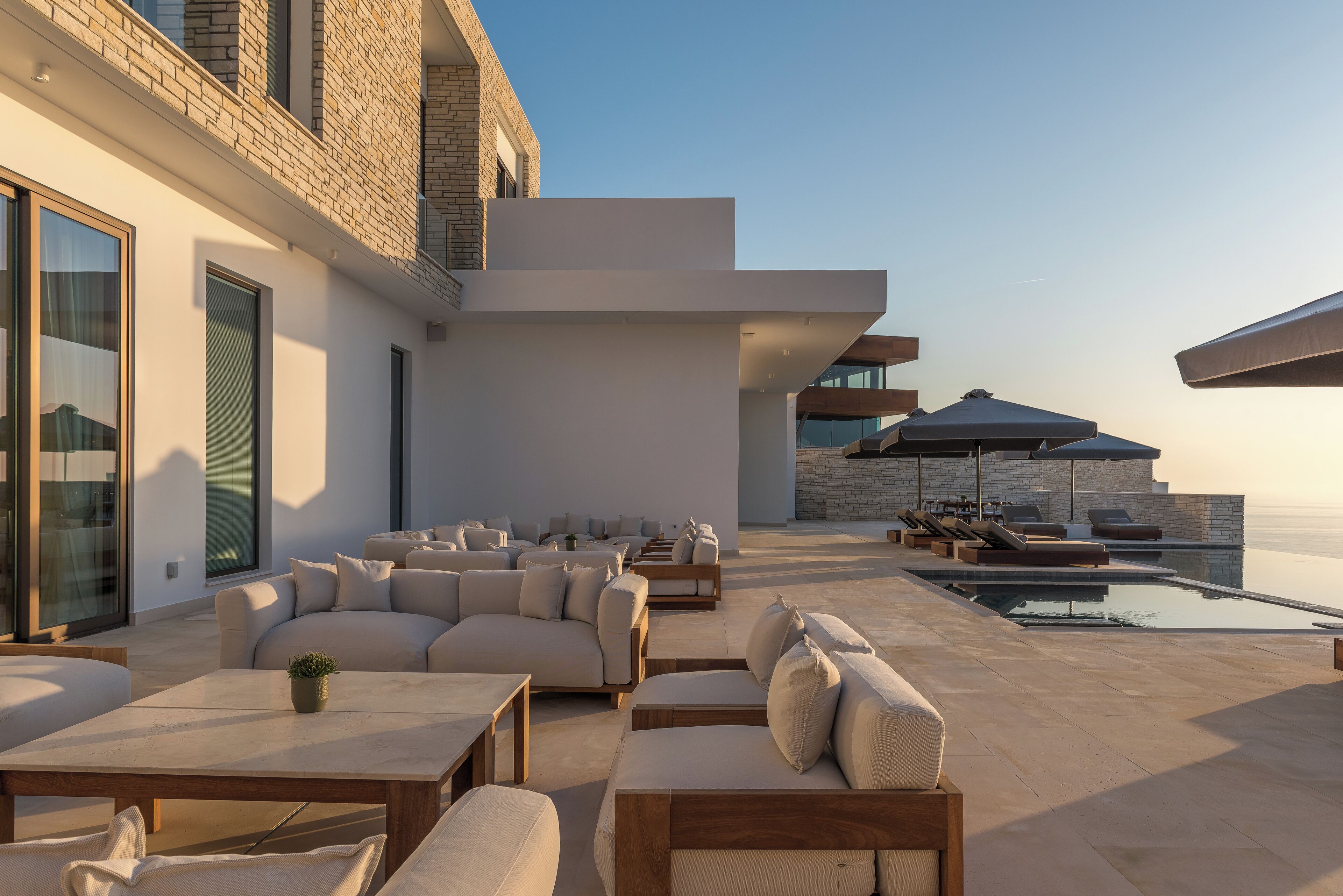 Un espace de détente extérieur moderne, doté de nombreux sièges, d’une piscine et offrant une vue dégagée sur l’océan.