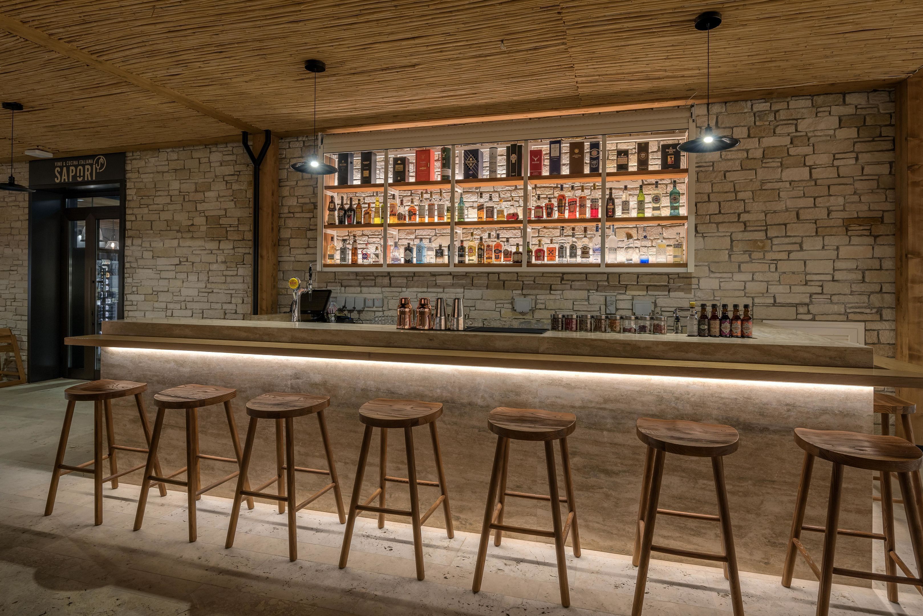 Zona de bar con taburetes de madera, pared de ladrillo y estantes llenos de botellas.