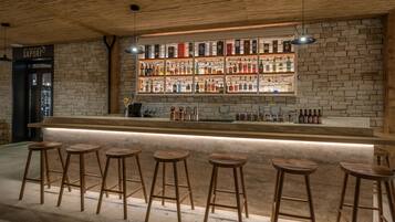 Zona de bar con taburetes de madera, pared de ladrillo y estantes llenos de botellas.