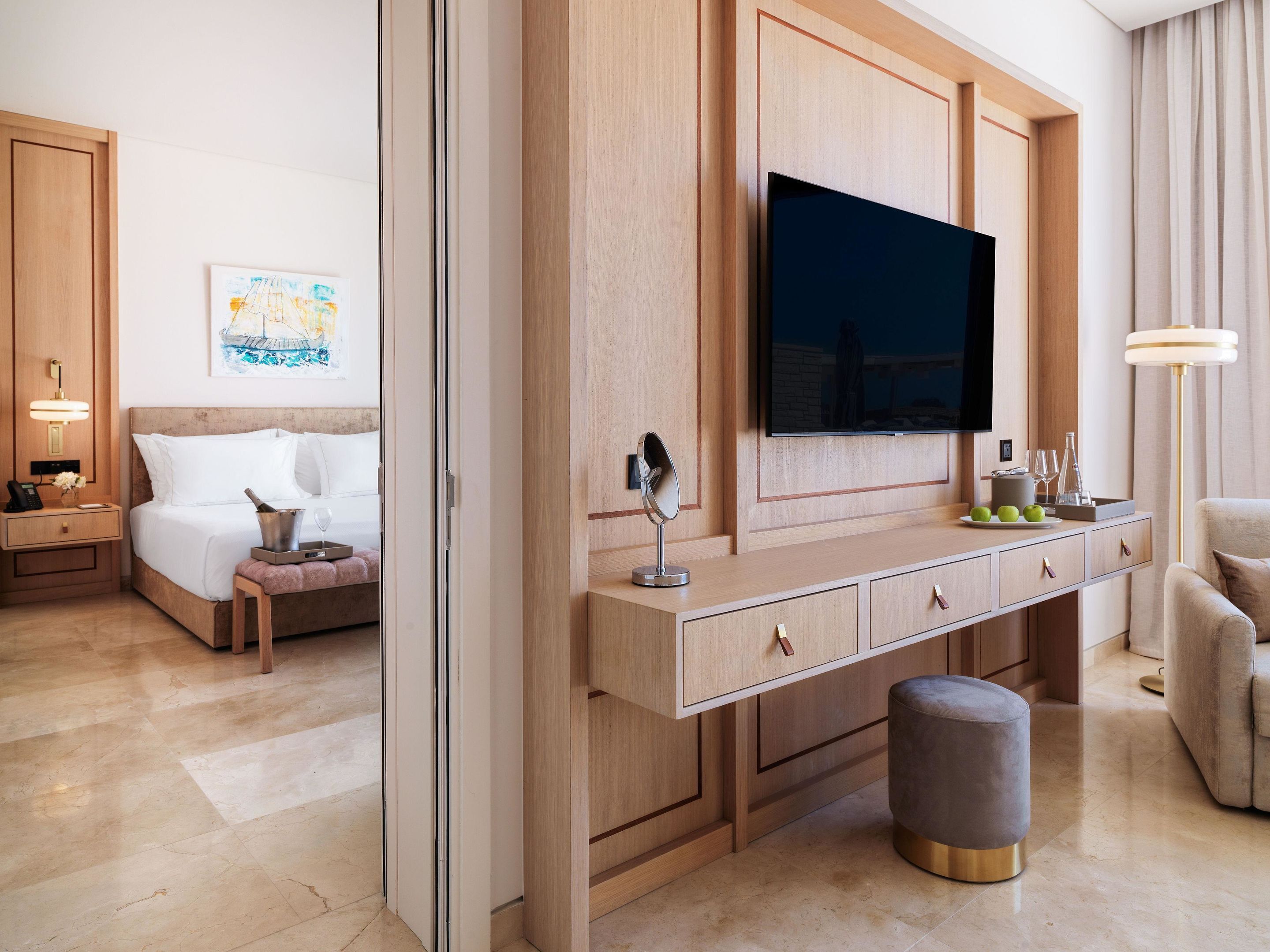 A modern hotel room with a bed, bedside table, lamp, and a flat-screen TV mounted on the wall.