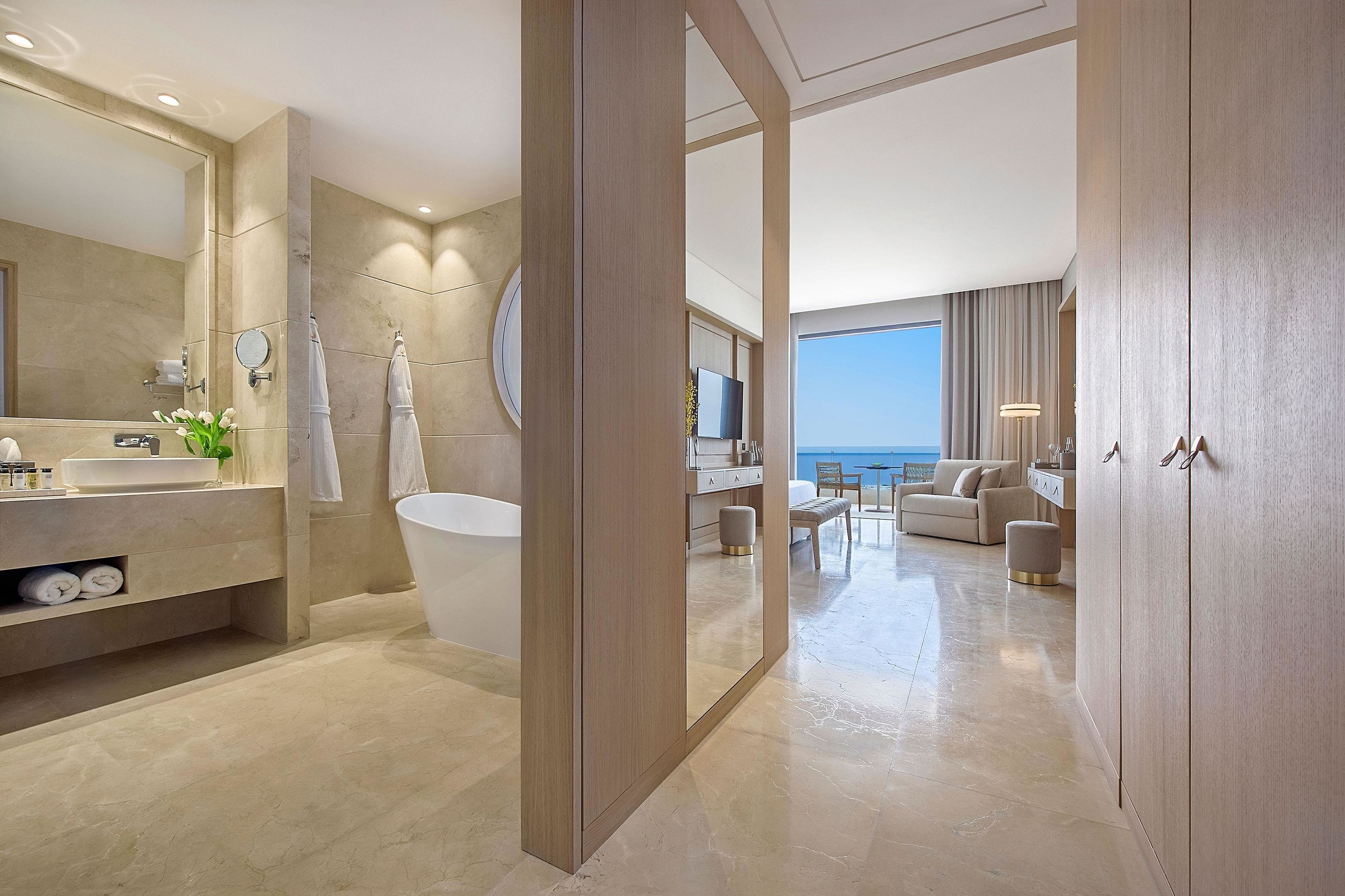 A modern bathroom with a large mirror, a bathtub, and a vanity with a sink and toiletries.
