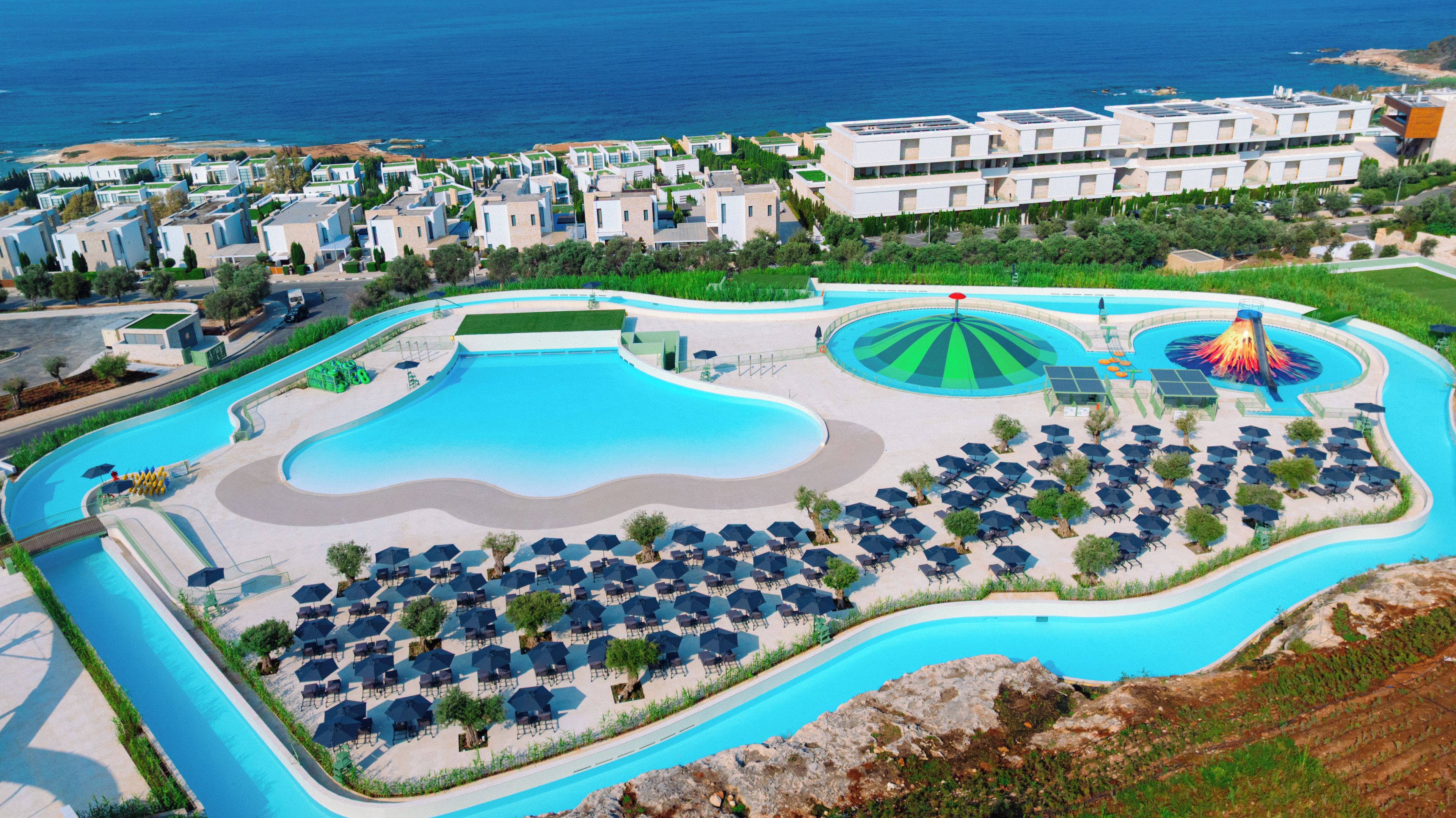 A resort with a large pool, sun loungers, and a view of the sea.