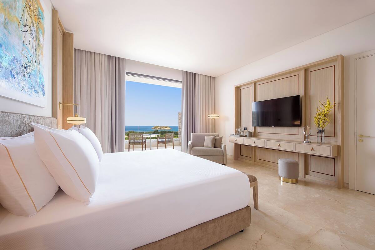 Une chambre d’hôtel avec un grand lit, un bureau, une télévision et une vue sur l’océan.