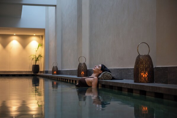 A person relaxing in a pool with warm lighting and decorative lanterns.