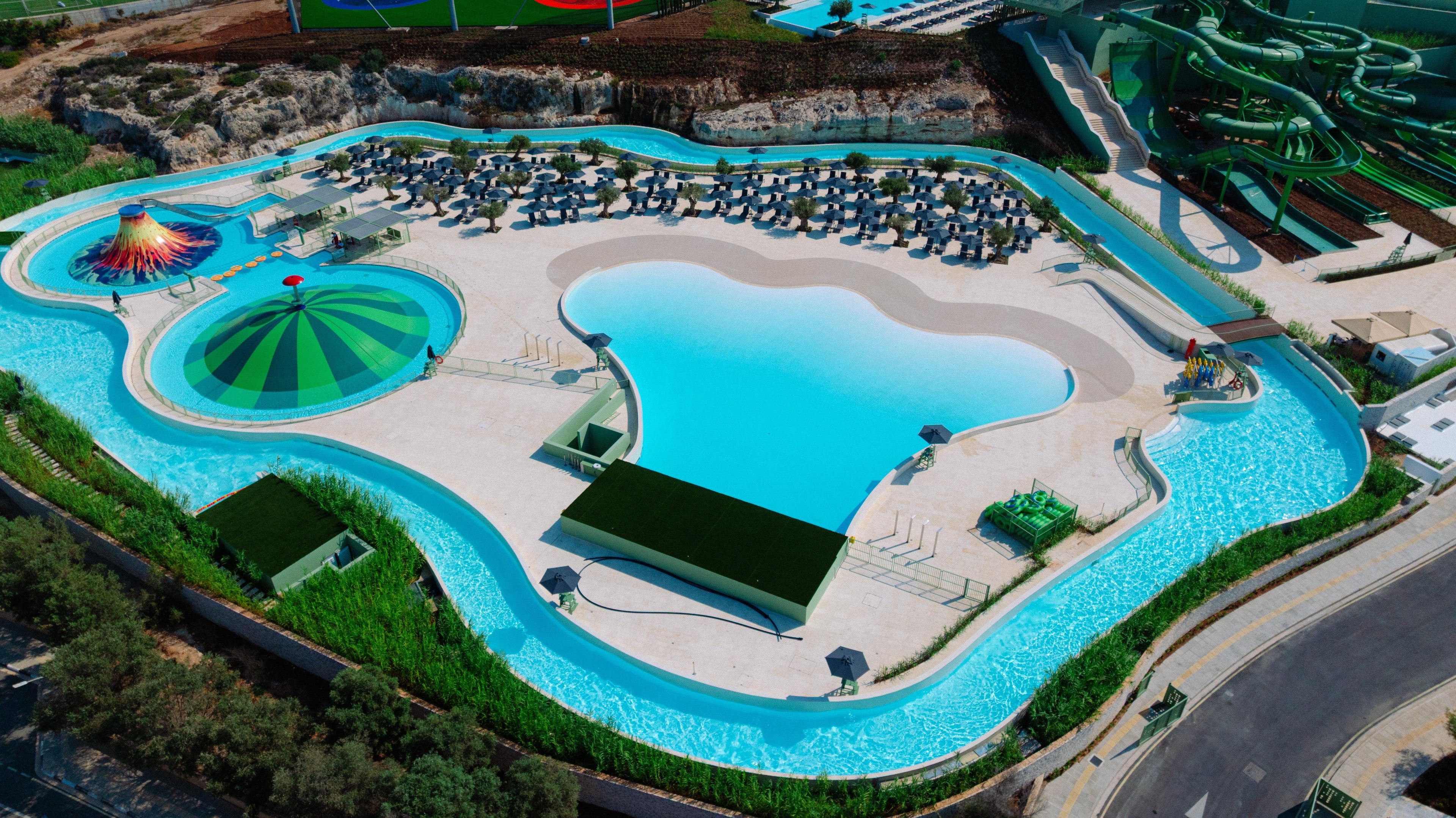 An aerial view of a resort with multiple swimming pools, sun loungers, and a water slide.