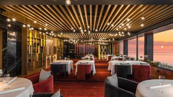 Um restaurante com um espaço amplo para refeições, várias mesas e vista para o pôr do sol.