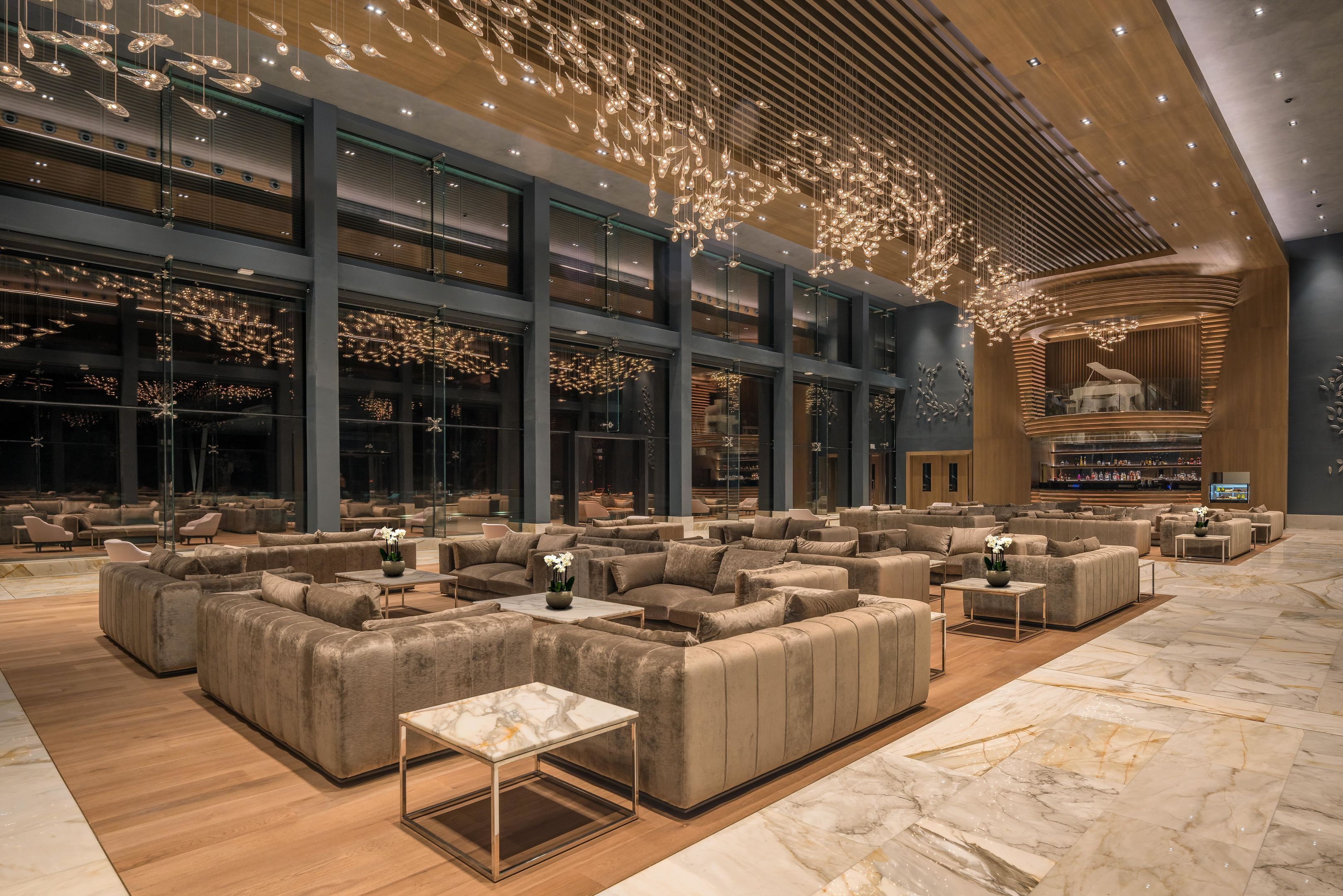 A spacious lobby with multiple seating areas, large windows, and a modern chandelier.