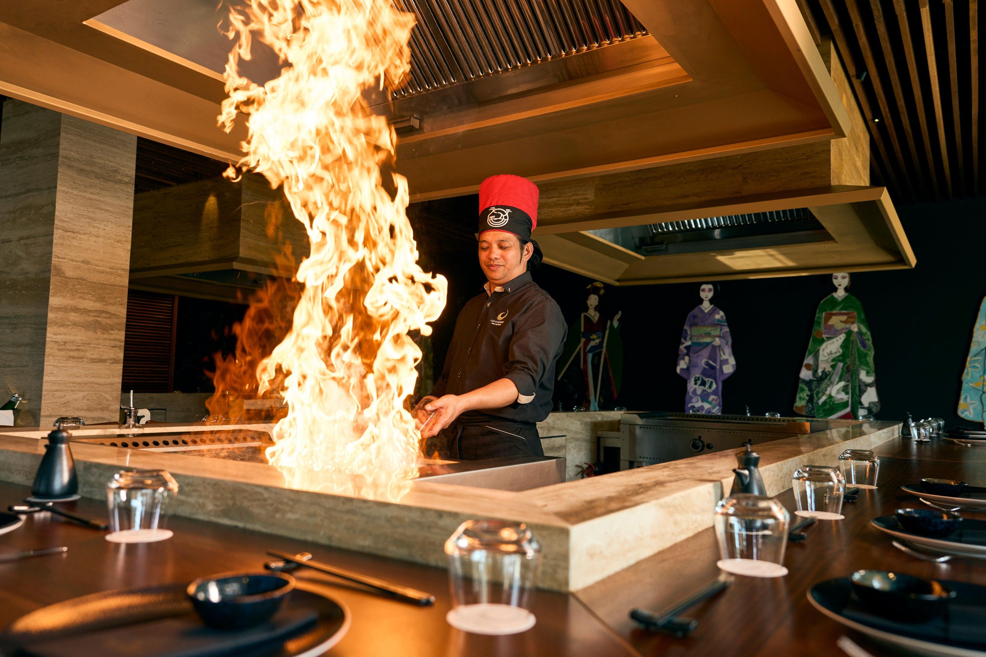 A chef performing a flambé at a restaurant counter with a modern interior design.
