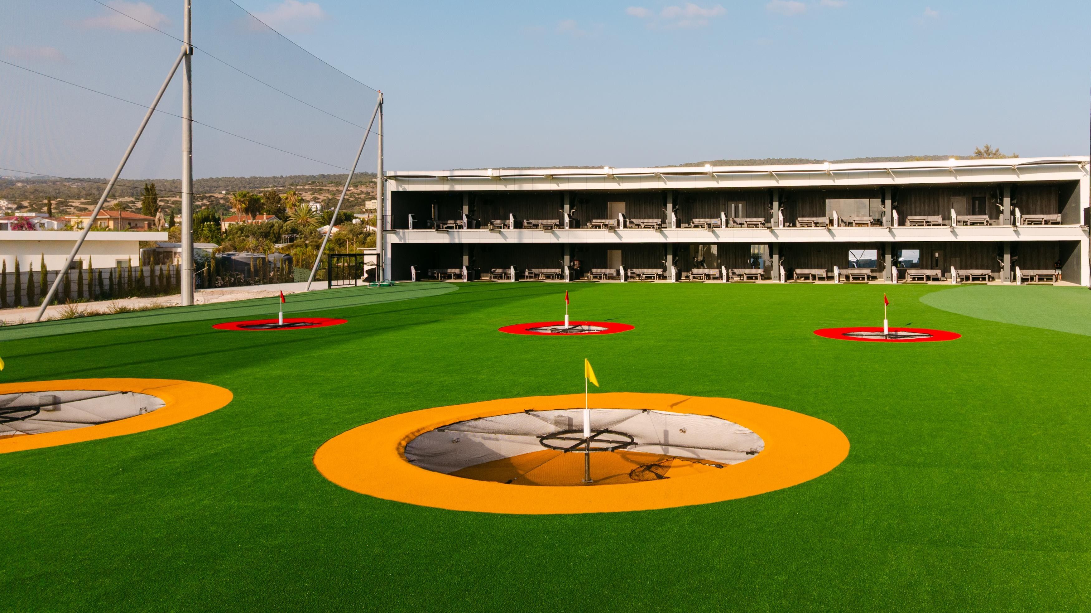 A golf course with multiple putting greens, a building with multiple floors, and a clear sky.