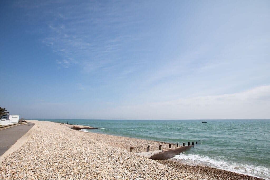 A pebble beach with a concrete walkway and a pier extending into the sea.