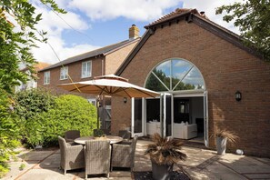 A brick house with a patio, outdoor furniture, and a large window. - West Wittering Beach House for 6 (West Wittering)