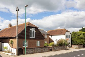 A residential street with two houses, one with a brick facade and the other with a white exterior, both featuring pitched roofs and visible chimneys.