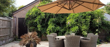 Een terras met rieten meubels, een potplant en een grote parasol.
