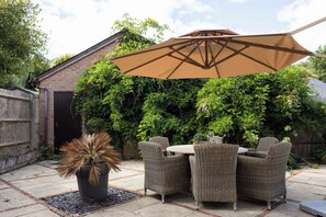 A patio with wicker furniture, a potted plant, and a large umbrella.