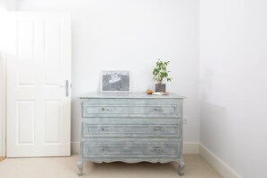 A light blue dresser with drawers, a framed picture, and a potted plant against a white wall. - West Wittering Beach House for 6 (West Wittering)