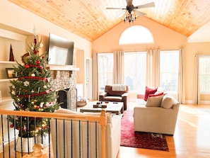 Uma sala de estar acolhedora com lareira, árvore de Natal e uma janela grande com cortinas.