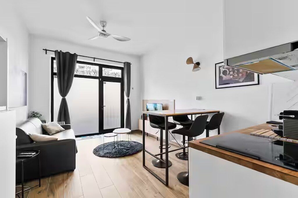 A modern living space with a sofa, a dining table with chairs, a ceiling fan, and a large window with curtains.