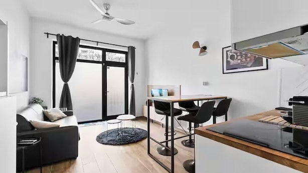 A modern living space with a sofa, a dining table with chairs, a ceiling fan, and a large window with curtains.