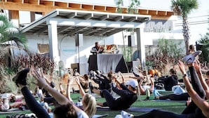 Un grupo de personas practicando yoga al aire libre con un orador en el escenario.
